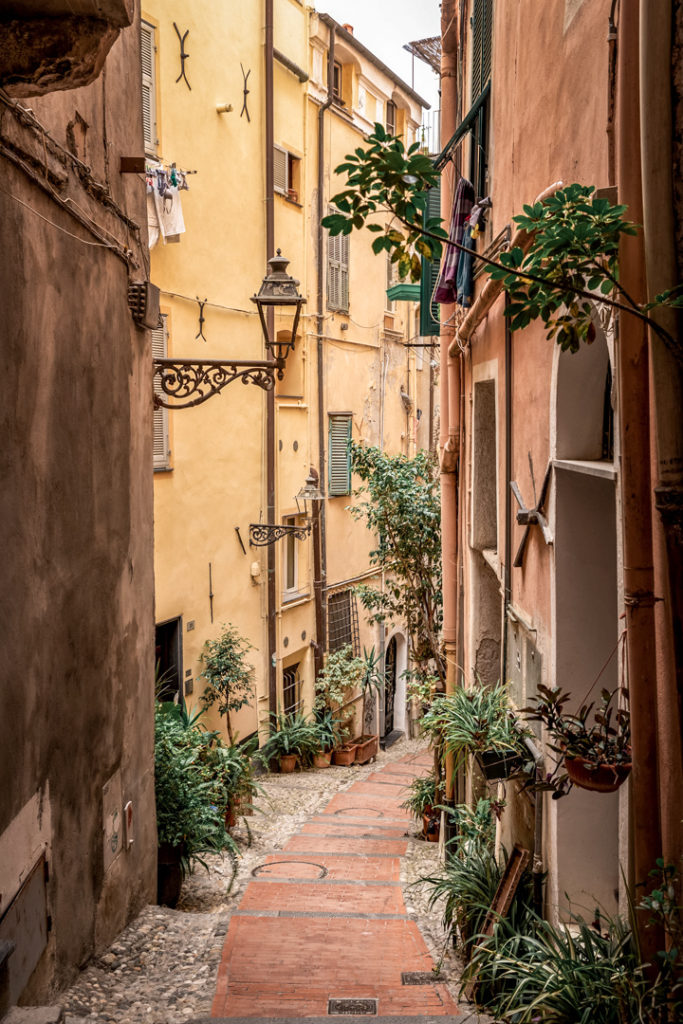 Rue étroite et colorée de La Pigna, vieille ville de Sanremo, Italie, avec des plantes vertes et des lampadaires en fer forgé.