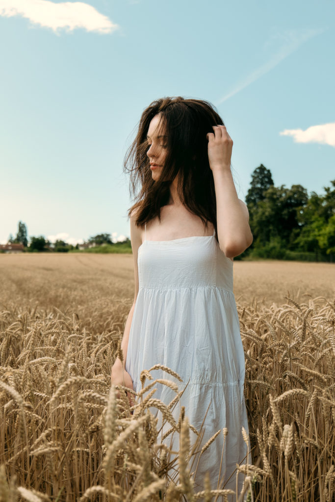 Jeune femme aux cheveux châtains en robe blanche dans un champ de blé sous une douce lumière matinale