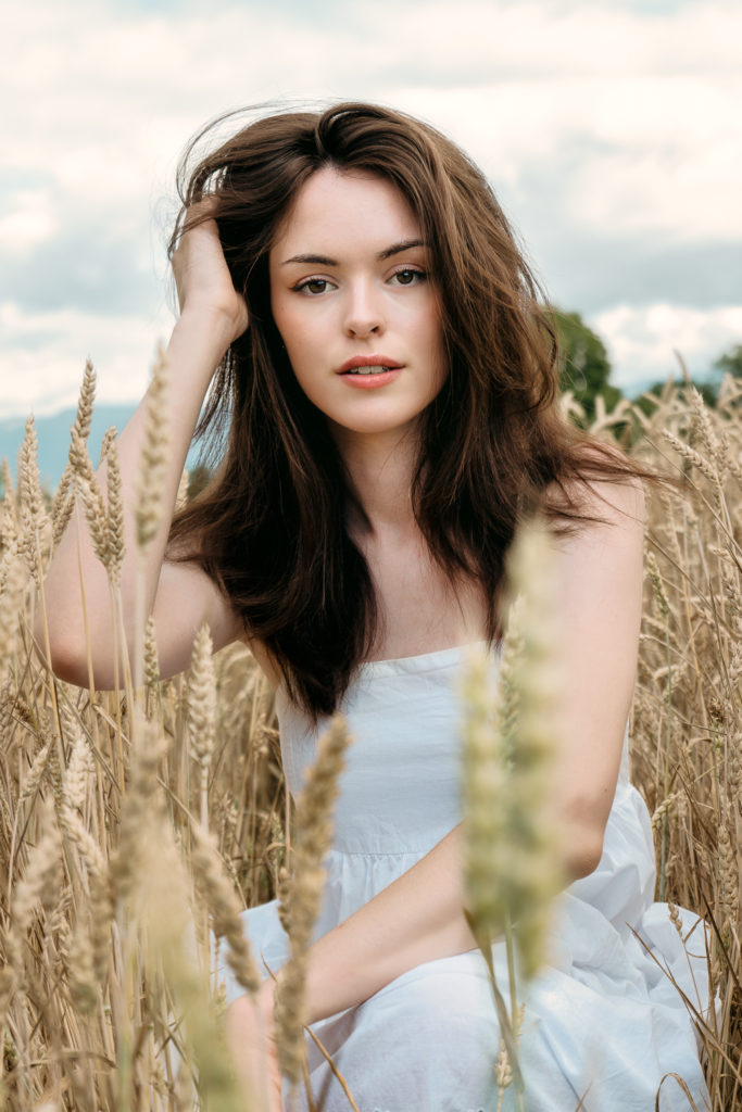 Young woman with chestnut hair in a white dress in a wheat field under a soft morning light