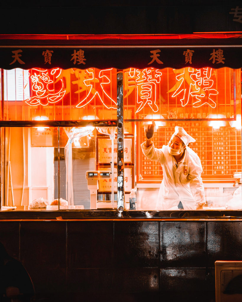 Local butcher shop in Tianjin illuminated at night with a worker inside