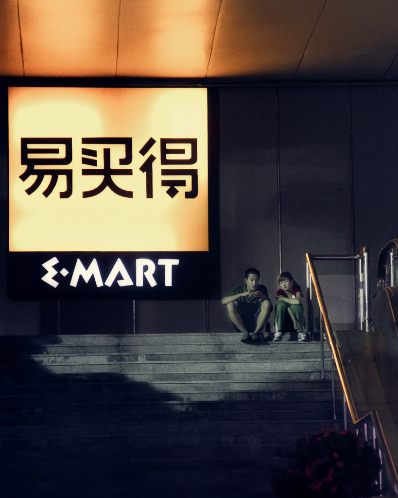 Neon sign of I.Marta supermarket in Tianjin with a young couple sitting in its shadow