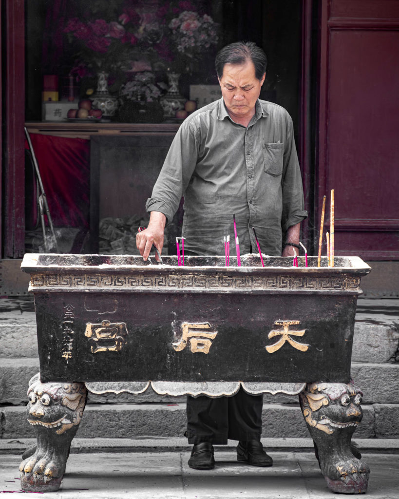 Un gardien de temple à Tianjin trie l'encens devant un bac en fonte, ses expressions rappelant un personnage d'opéra chinois.
