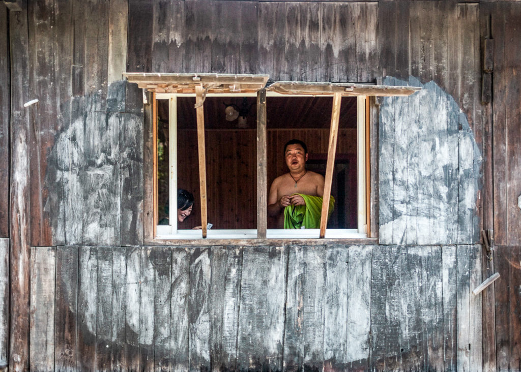 Scène locale de Wuzhen capturée depuis un bateau, montrant une habitation traditionnelle et un habitant saluant à la fenêtre.