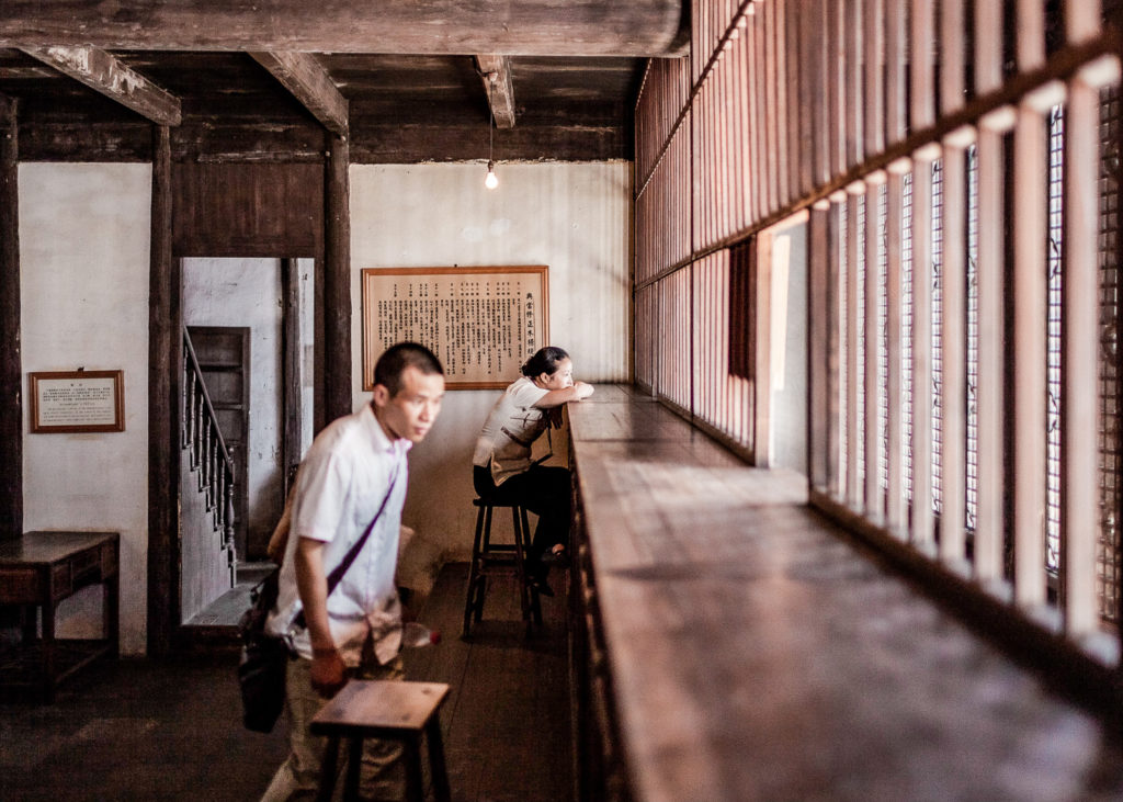 Guide leaning on the counter of an ancient inactive pawnshop in Wuzhen, with a blurred tourist exploring the interior, embodying a silent narrative of bygone days.