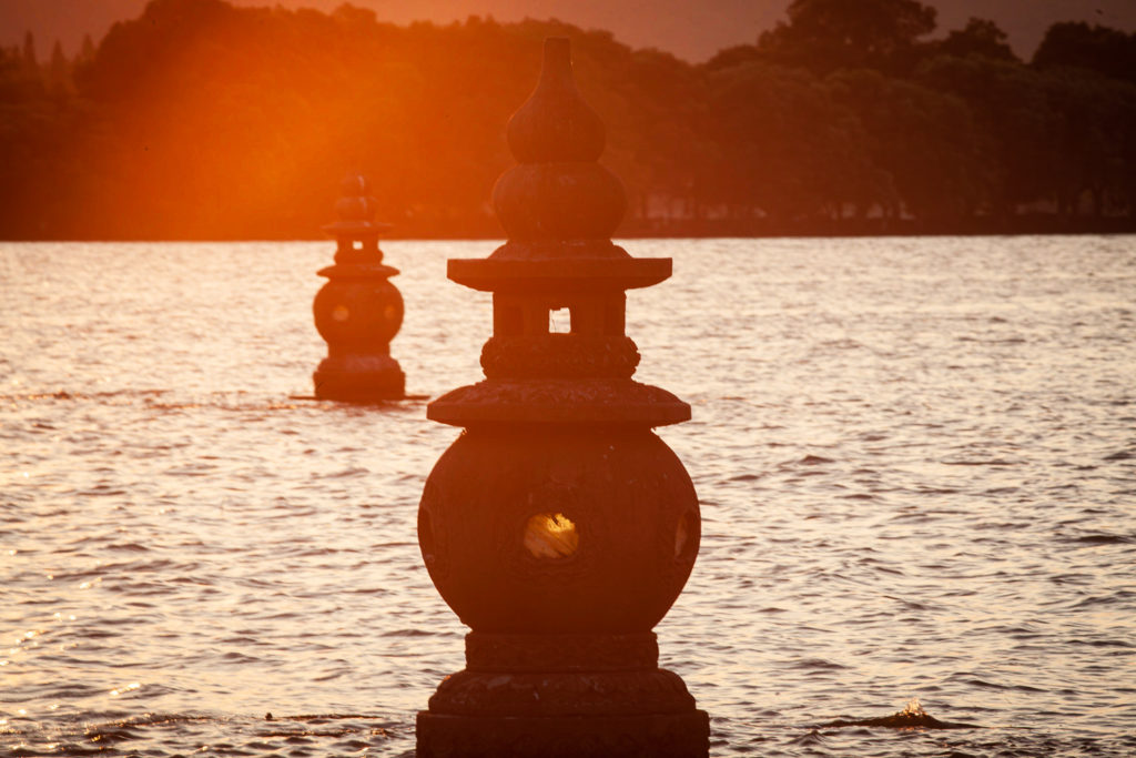 Deux pagodes en pierre émergeant du Lac de l'Ouest, baignées par la lumière dorée du soleil couchant.